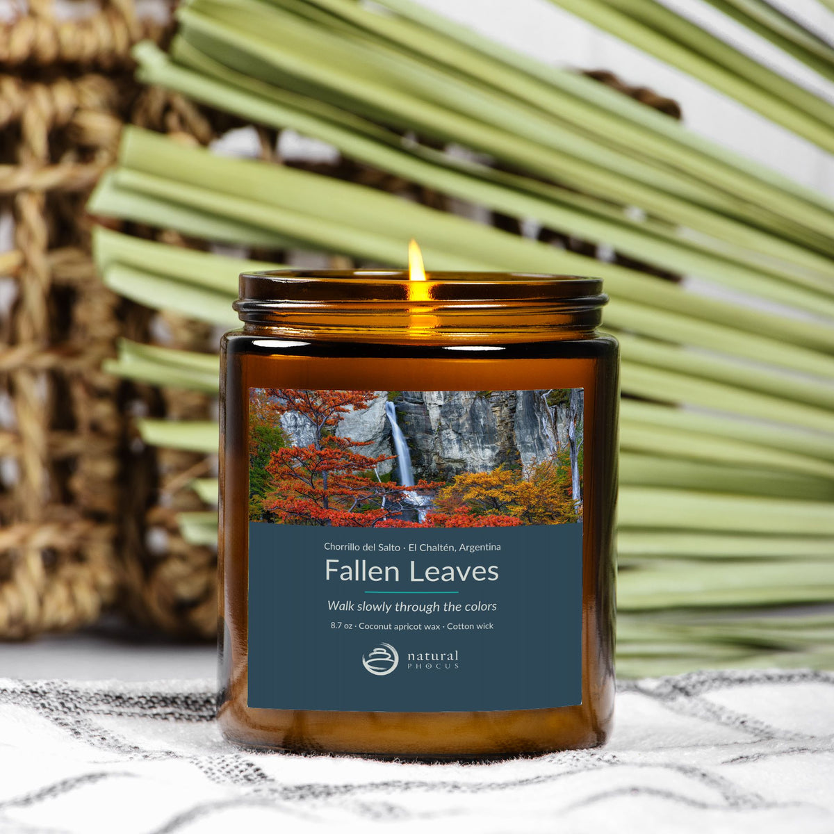 Chorrillo del Salto Candle in Fallen Leaves, an amber glass jar candle with a gold lid, labeled with a photograph of a waterfall framed by red and gold autumn trees near El Chaltén, Argentina