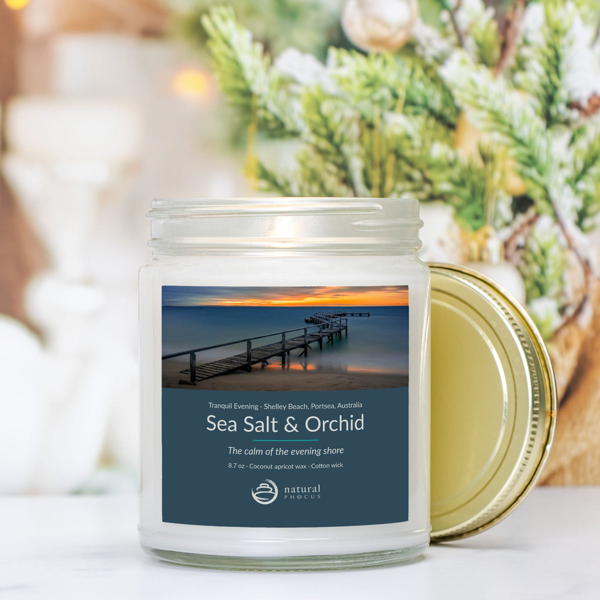 Tranquil Evening Candle in Sea Salt and Orchid, a clear glass jar candle with a gold lid, labeled with a photograph of a wooden jetty curving into still water at sunset at Shelley Beach, Portsea, Australia