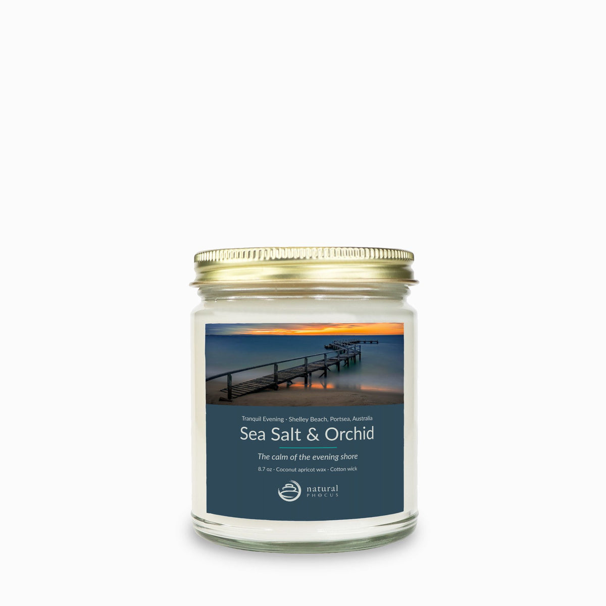 Tranquil Evening Candle in Sea Salt and Orchid, a clear glass jar candle with a gold lid, labeled with a photograph of a wooden jetty curving into still water at sunset at Shelley Beach, Portsea, Australia