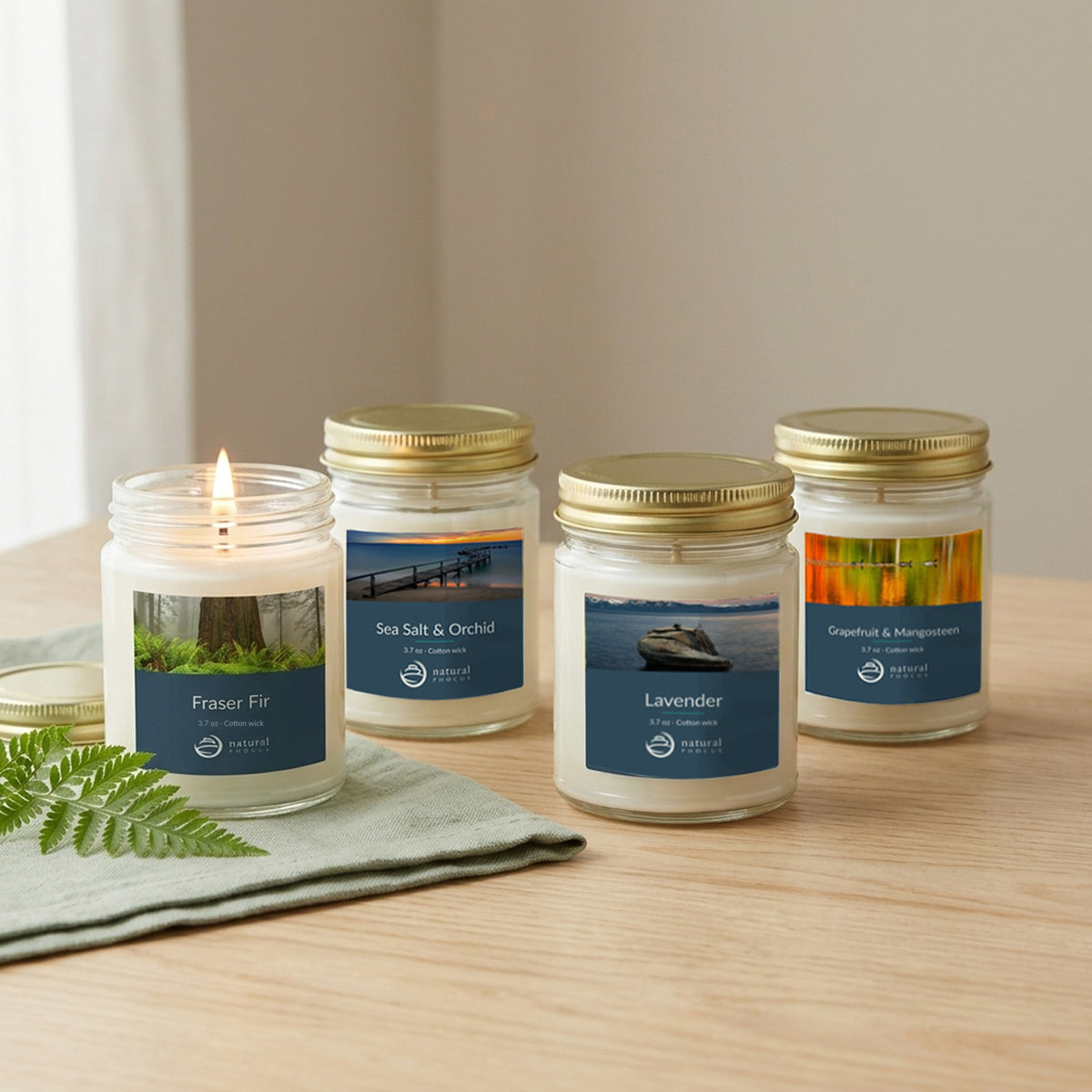 Everyday Discovery Set: four mini candles on a light wood table beside a sage linen napkin and a fern sprig, with the Fraser Fir candle lit