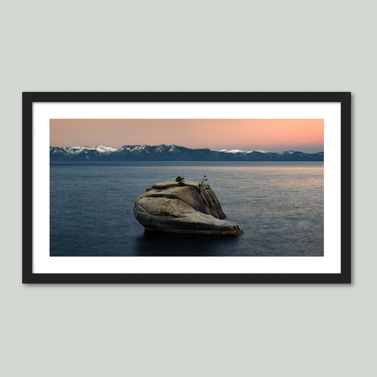 The Heart of Lake Tahoe, a solitary rock with a small tree rising from the still water of Lake Tahoe at sunrise, in a black frame with a white mat