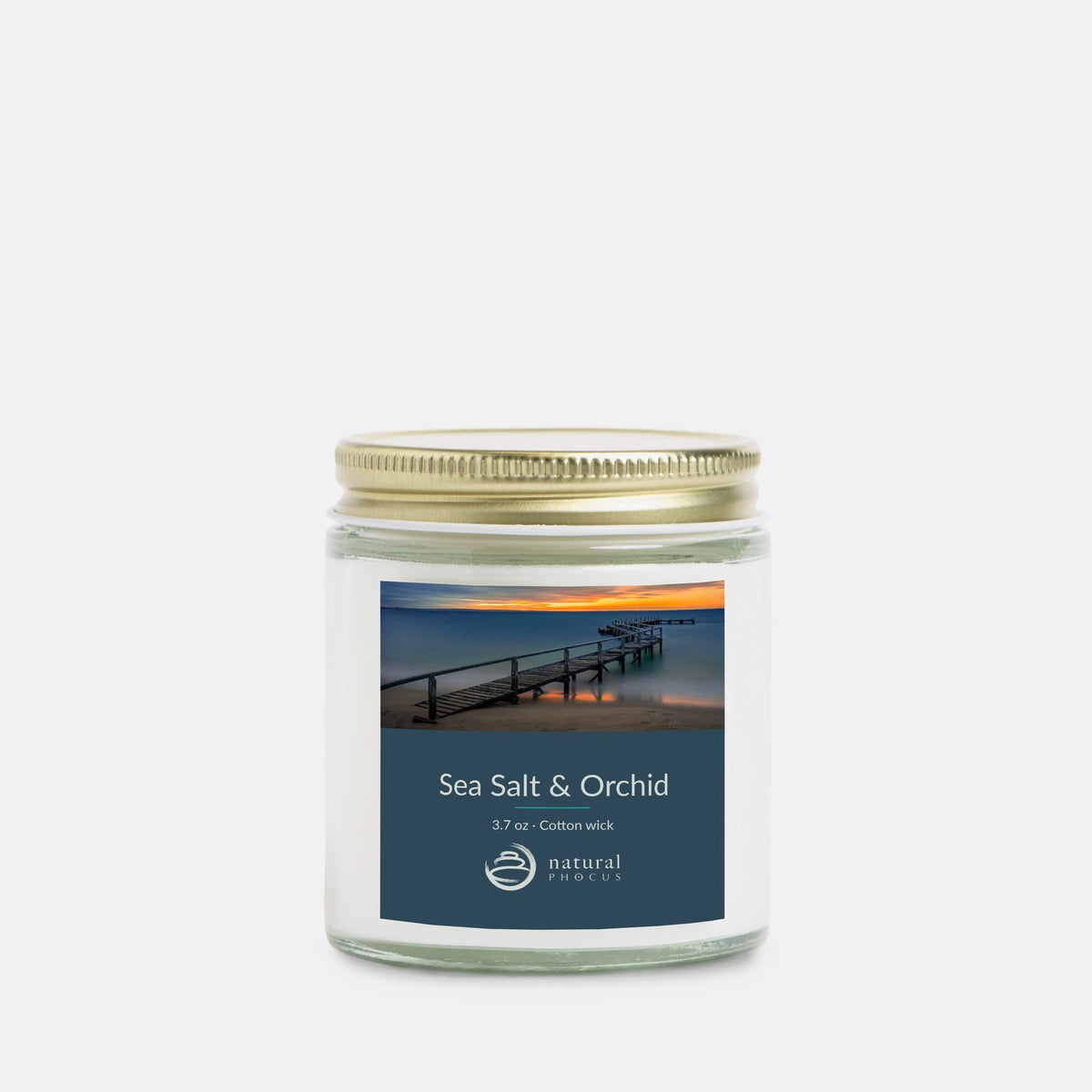 Tranquil Evening Mini Candle in Sea Salt and Orchid, a 4 oz clear glass jar candle with a gold lid, labeled with a photograph of a wooden jetty curving into still water at sunset at Shelley Beach, Portsea, Australia