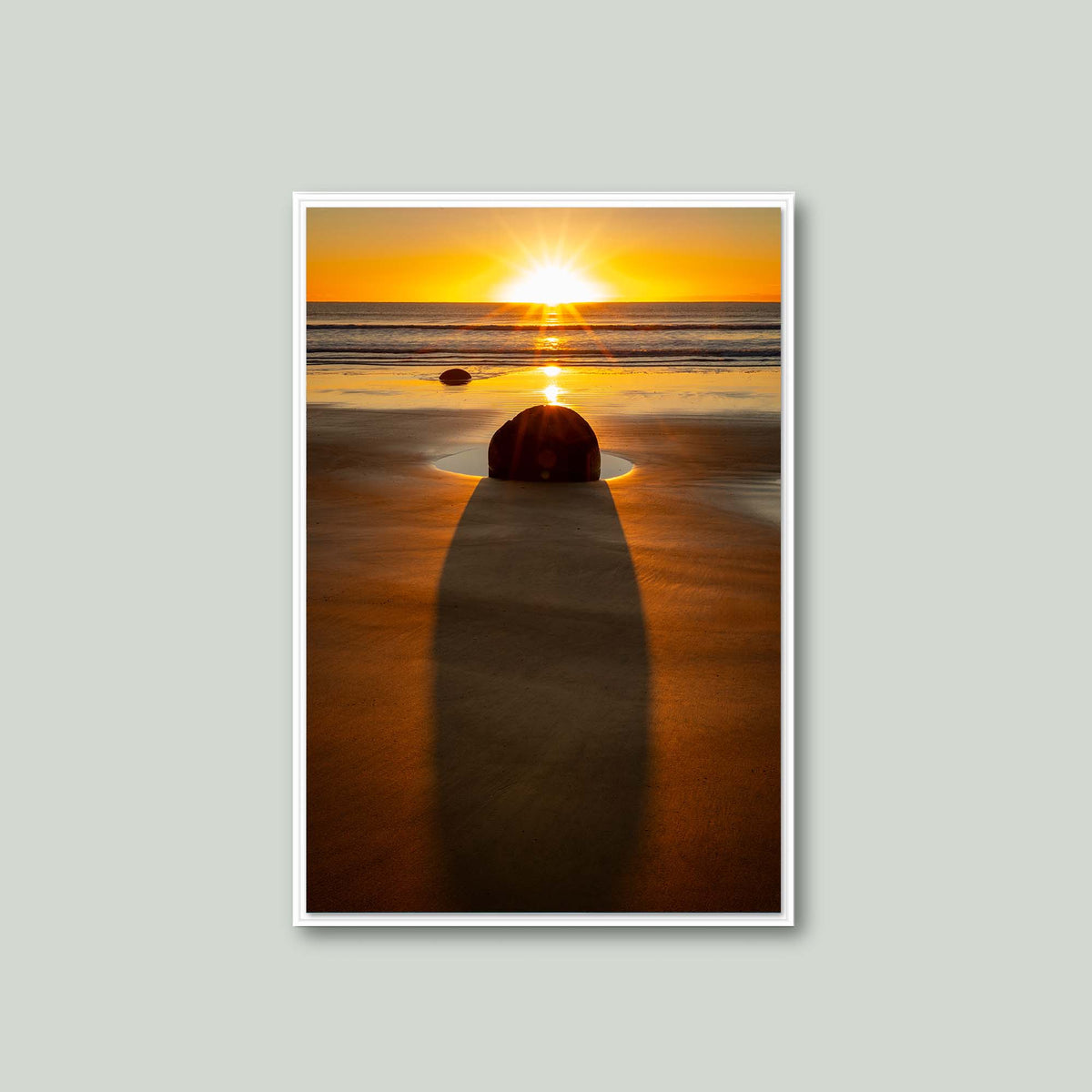 The Patient Stone, a Moeraki Boulder casting a long shadow toward the viewer as the sun rises over the Pacific in Otago, New Zealand, as a canvas in a white floating frame