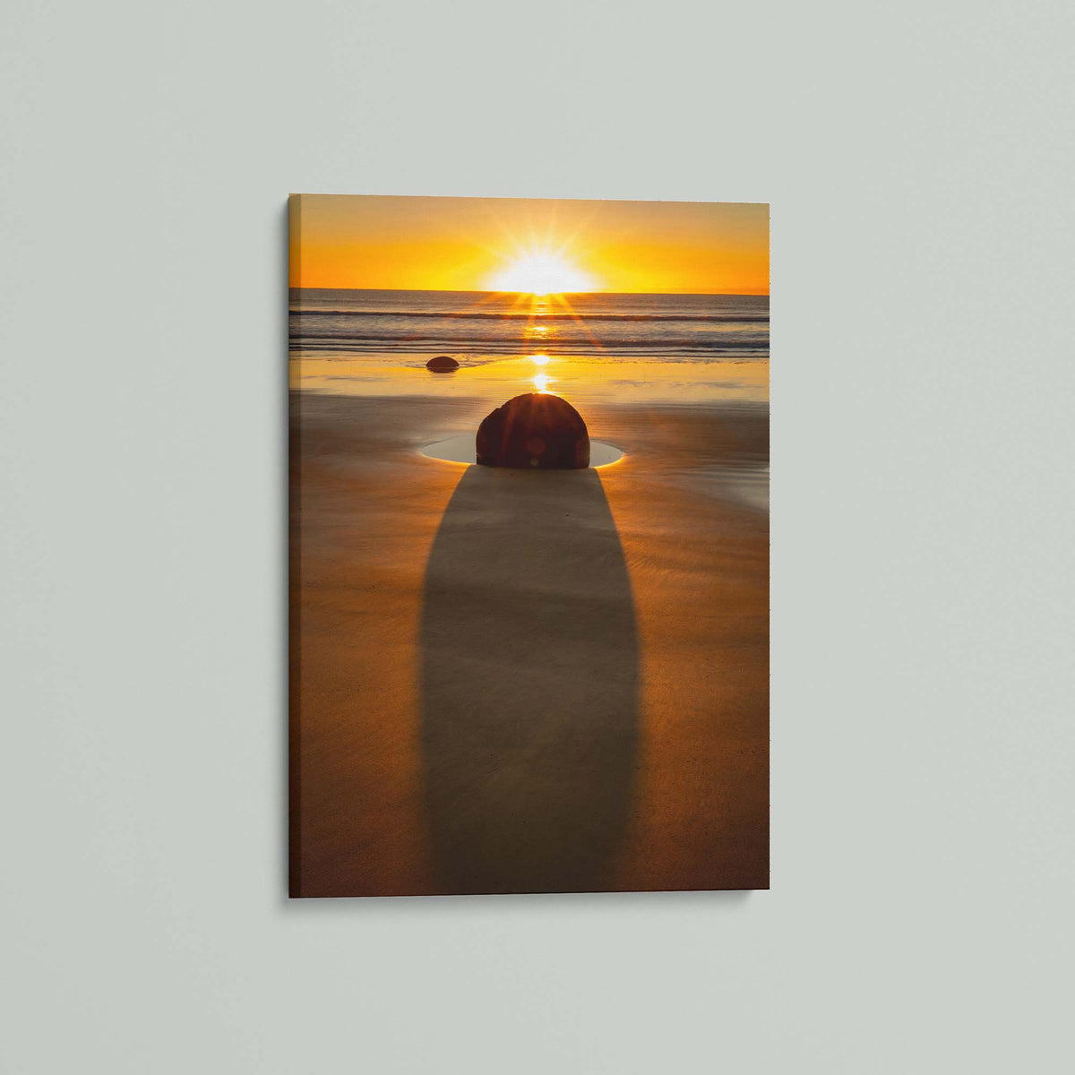 The Patient Stone, a Moeraki Boulder casting a long shadow toward the viewer as the sun rises over the Pacific in Otago, New Zealand, as a stretched canvas shown at an angle