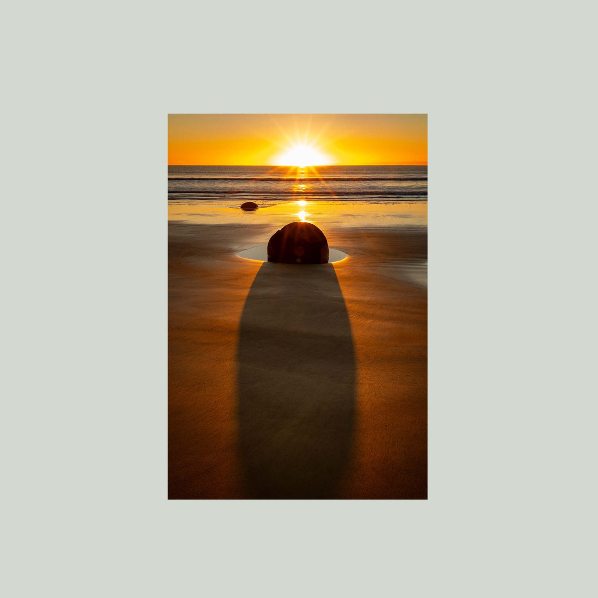 The Patient Stone, a Moeraki Boulder casting a long shadow toward the viewer as the sun rises over the Pacific in Otago, New Zealand, as an unframed print