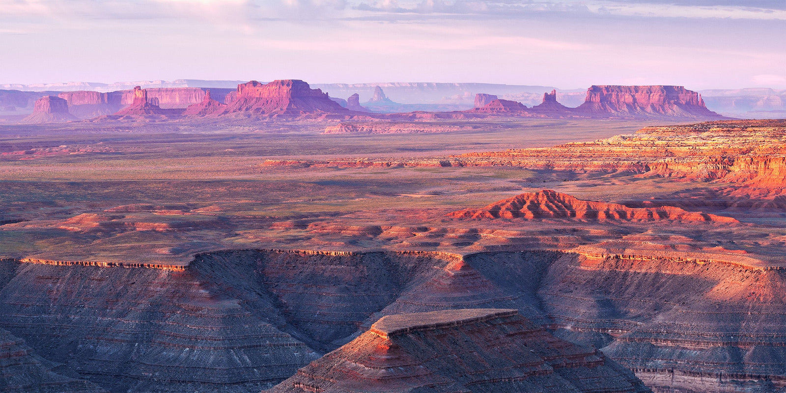 Sunrise light on the distant buttes of Monument Valley seen from the canyon rim at Muley Point, Utah