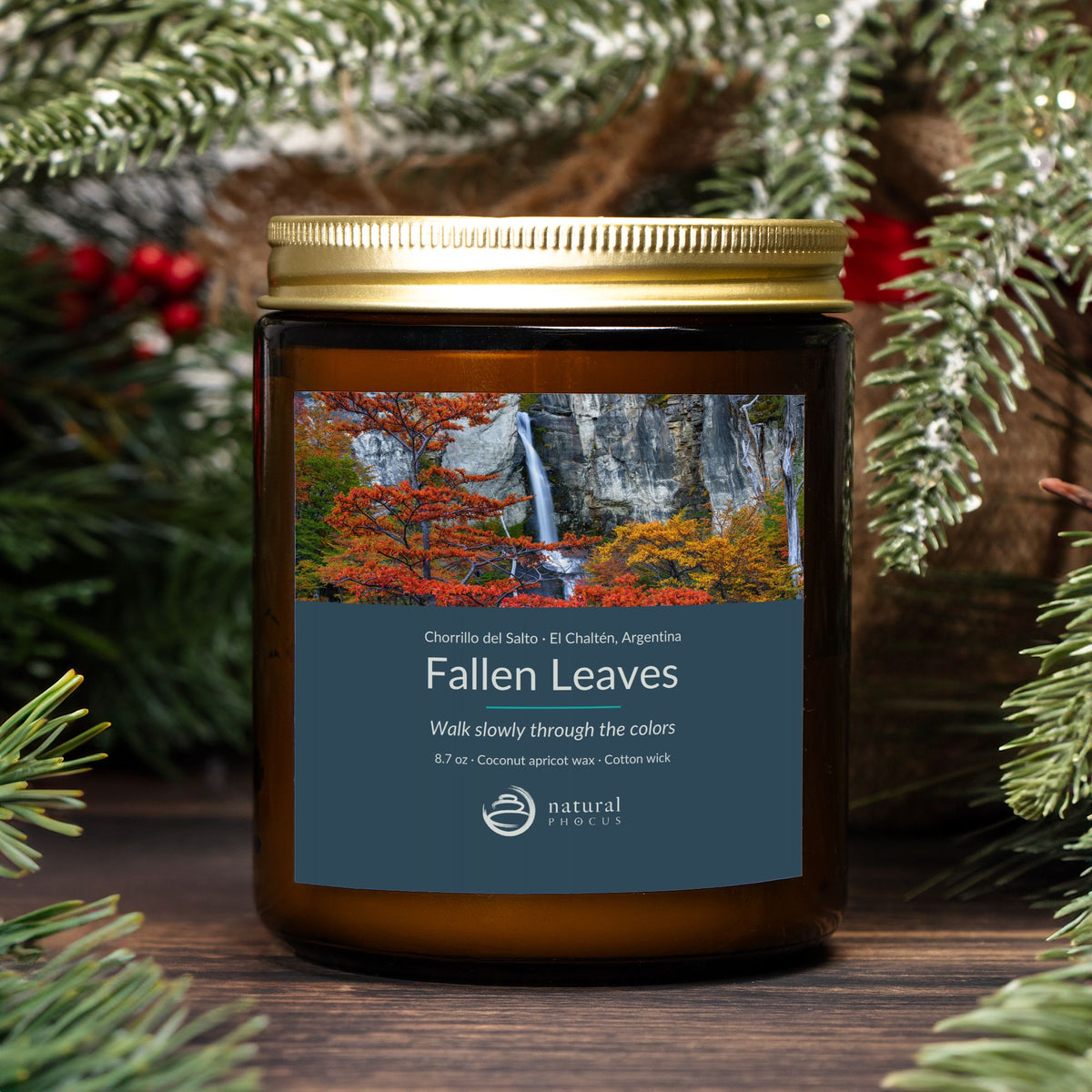 Chorrillo del Salto Candle in Fallen Leaves, an amber glass jar candle with a gold lid, labeled with a photograph of a waterfall framed by red and gold autumn trees near El Chaltén, Argentina