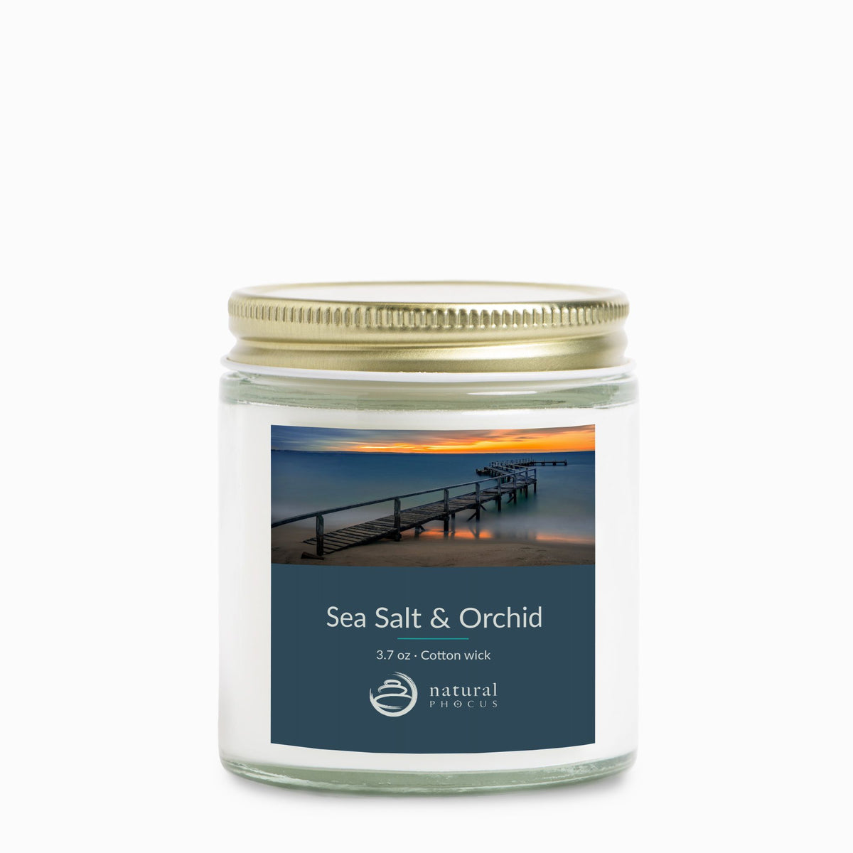Tranquil Evening Mini Candle in Sea Salt and Orchid, a 4 oz clear glass jar candle with a gold lid, labeled with a photograph of a wooden jetty curving into still water at sunset at Shelley Beach, Portsea, Australia