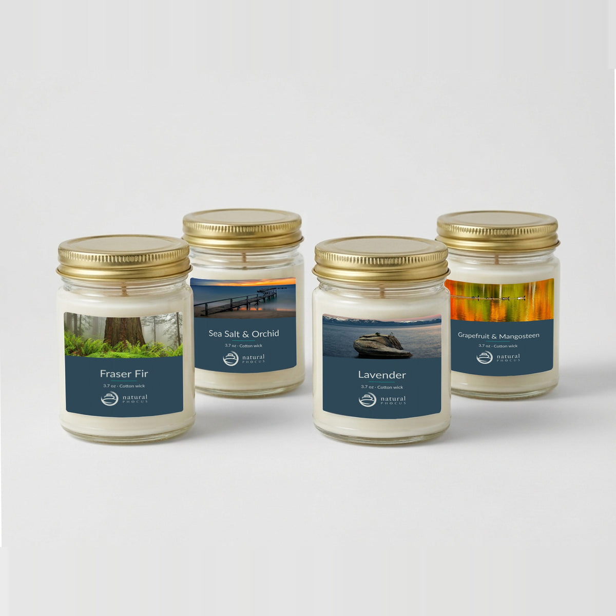 Everyday Discovery Set: four 4 oz clear glass mini candles with gold lids and navy labels, in Fraser Fir, Sea Salt and Orchid, Lavender, and Grapefruit and Mangosteen, each labeled with a landscape photograph