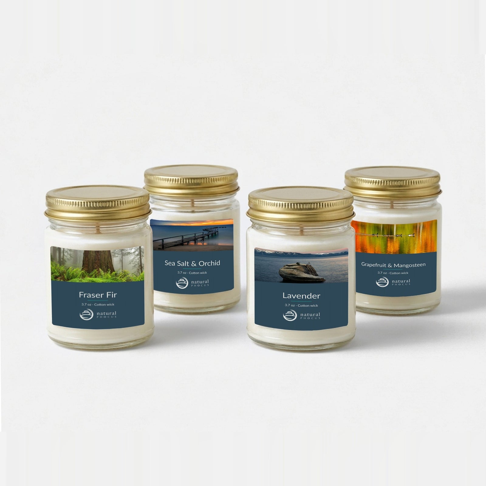 Everyday Discovery Set: four 4 oz clear glass mini candles with gold lids and navy labels, in Fraser Fir, Sea Salt and Orchid, Lavender, and Grapefruit and Mangosteen, each labeled with a landscape photograph