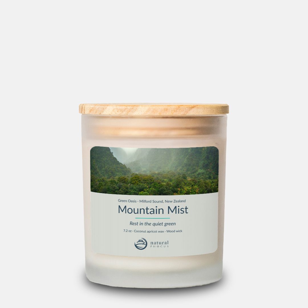Green Oasis Candle in Mountain Mist, a frosted glass candle with a maple wood lid, labeled with a photograph of mist drifting through a rainforest valley at Milford Sound, New Zealand