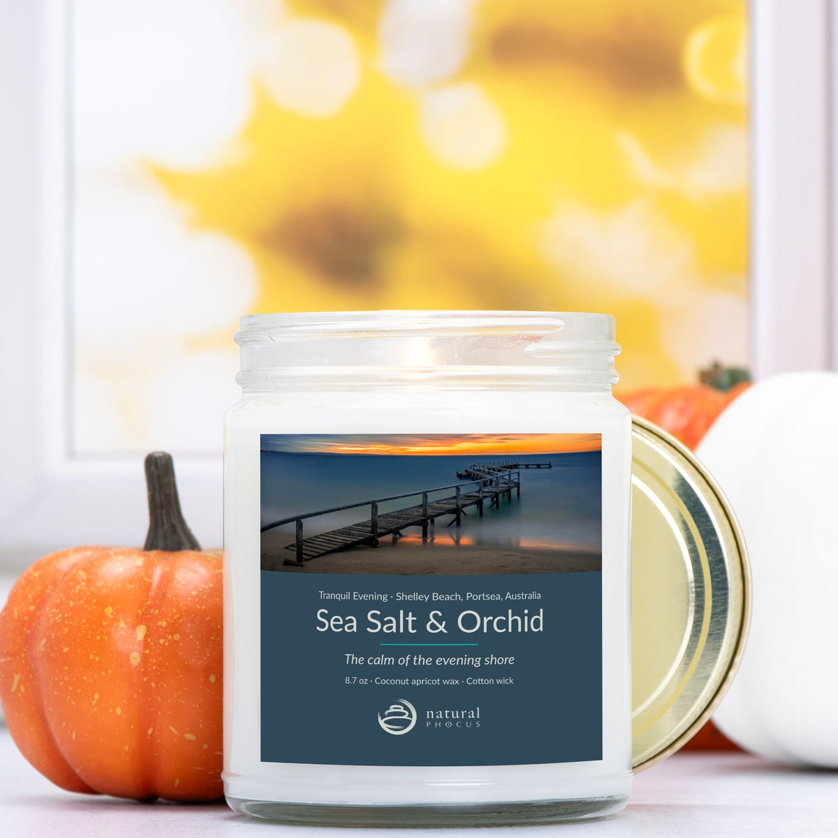 Tranquil Evening Candle in Sea Salt and Orchid, a clear glass jar candle with a gold lid, labeled with a photograph of a wooden jetty curving into still water at sunset at Shelley Beach, Portsea, Australia