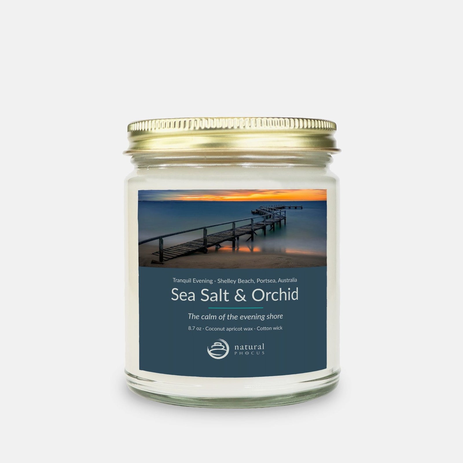 Tranquil Evening Candle in Sea Salt and Orchid, a clear glass jar candle with a gold lid, labeled with a photograph of a wooden jetty curving into still water at sunset at Shelley Beach, Portsea, Australia