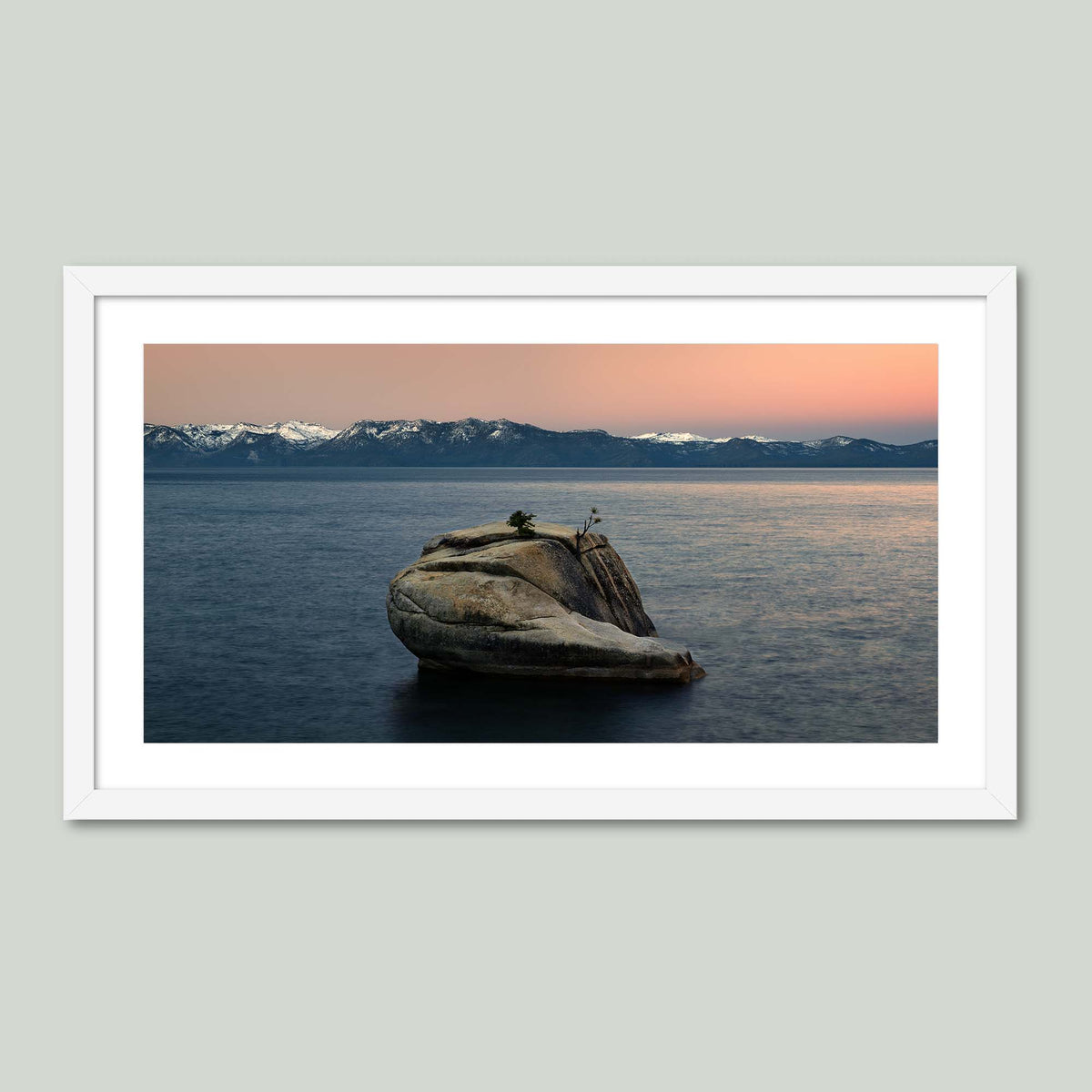 The Heart of Lake Tahoe, a solitary rock with a small tree rising from the still water of Lake Tahoe at sunrise, in a white frame with a white mat