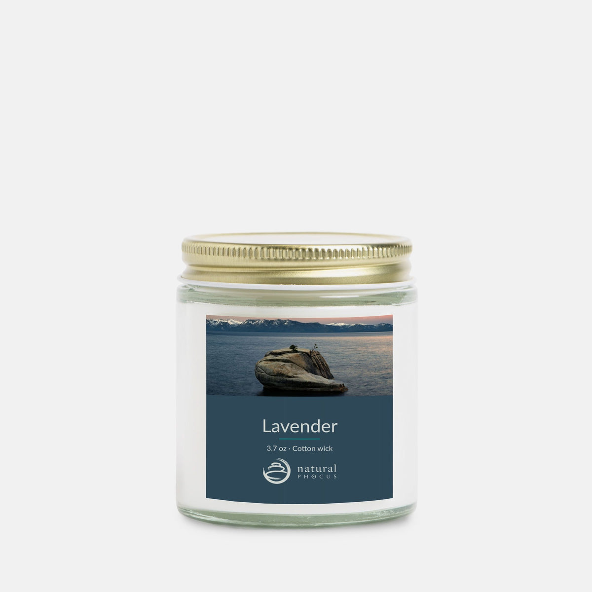 The Heart of Lake Tahoe Mini Candle in Lavender, a 4 oz clear glass jar candle with a gold lid, labeled with a photograph of Bonsai Rock in still water beneath snow-covered peaks at Lake Tahoe, Nevada