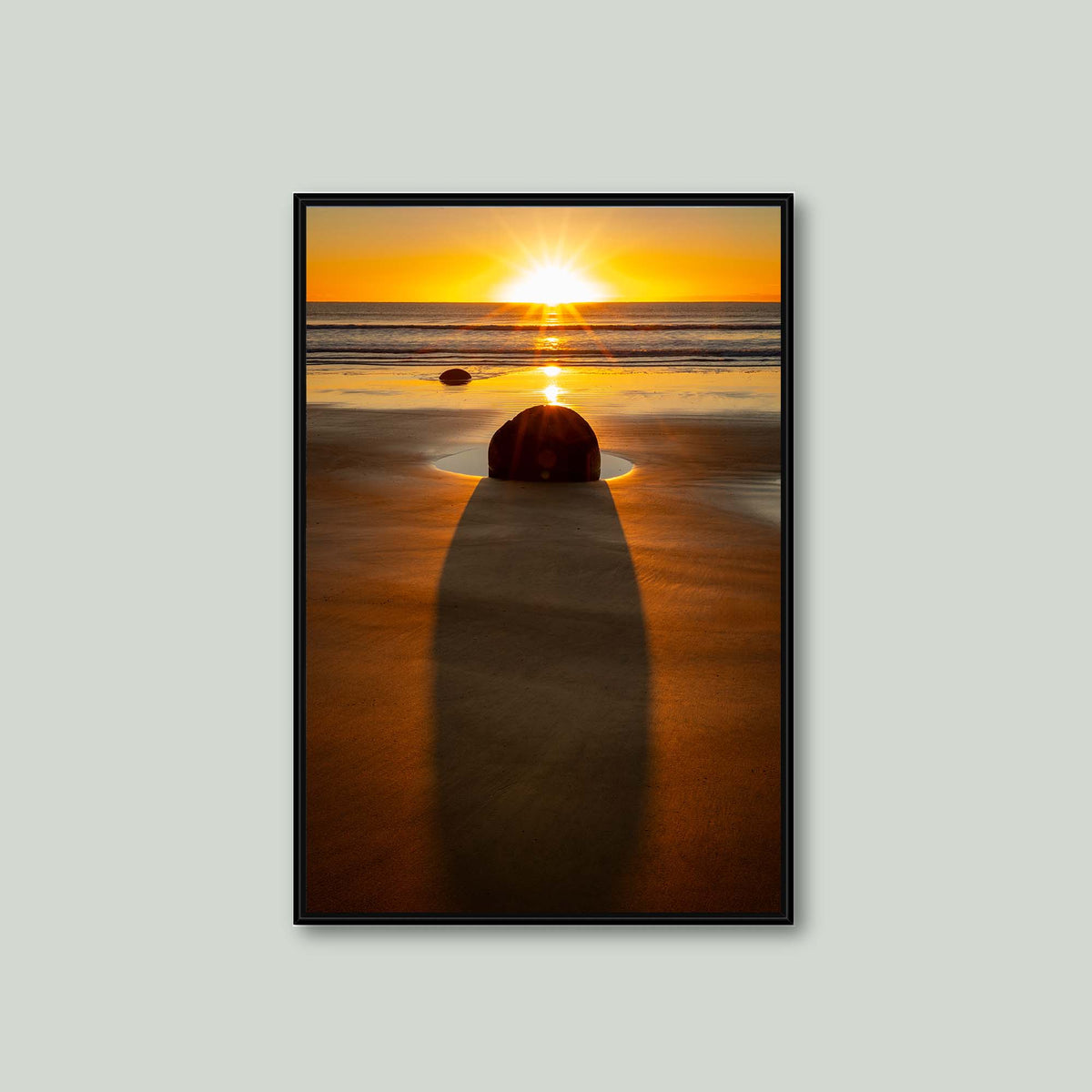 The Patient Stone, a Moeraki Boulder casting a long shadow toward the viewer as the sun rises over the Pacific in Otago, New Zealand, as a canvas in a black floating frame