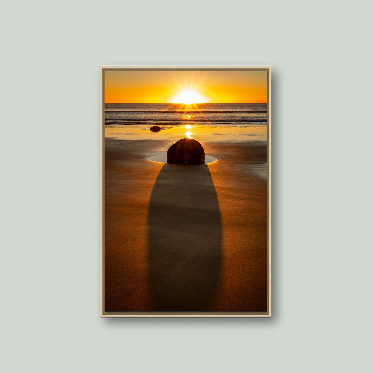 The Patient Stone, a Moeraki Boulder casting a long shadow toward the viewer as the sun rises over the Pacific in Otago, New Zealand, as a canvas in a maple floating frame