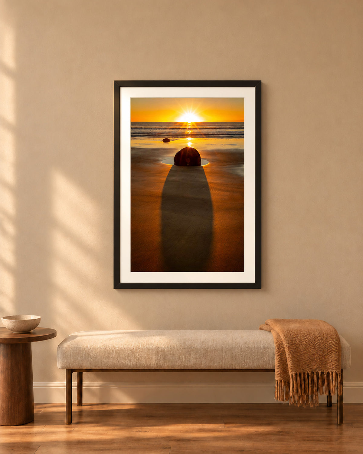 The Patient Stone, a Moeraki Boulder casting a long shadow as the sun rises over the Pacific in Otago, New Zealand, in a black frame shown in a home setting