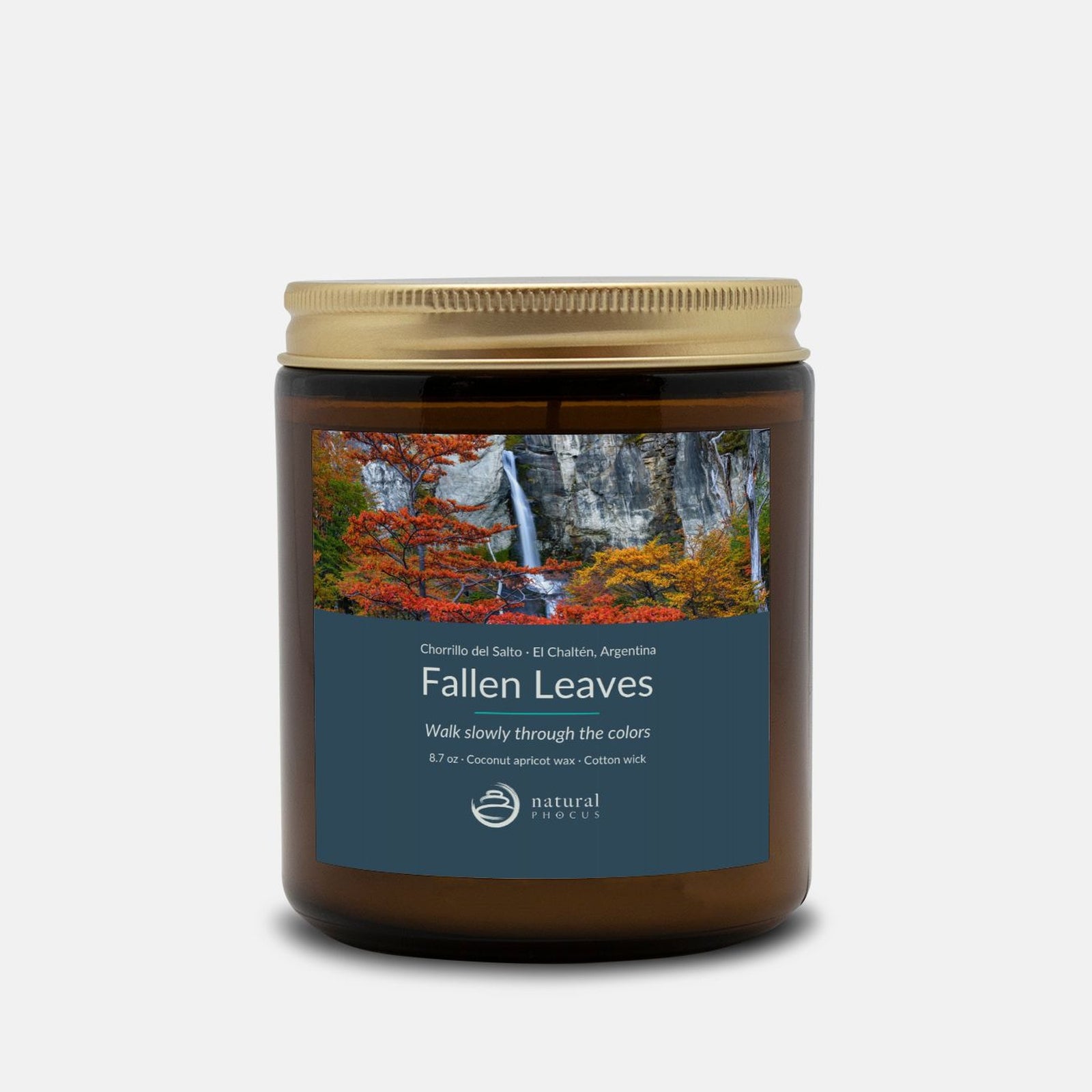 Chorrillo del Salto Candle in Fallen Leaves, an amber glass jar candle with a gold lid, labeled with a photograph of a waterfall framed by red and gold autumn trees near El Chaltén, Argentina